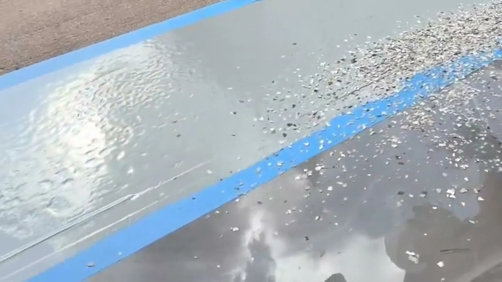 Colored flake being broadcast onto a wet epoxy coat next to blue tape